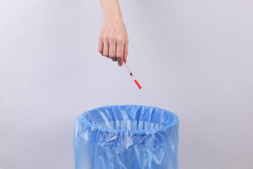 Hand throws syringe into trash bin with package on gray background