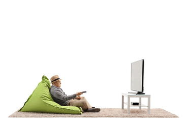 Full length shot of a senior gentleman with a remote controller sitting on a bean-bag chair and watching tv