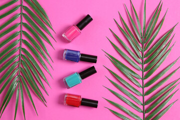 Bottles of nail polish and palm leaves on pink background. Beauty still life. Top view. Flat lay