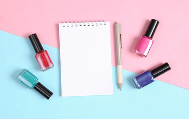 Bottles of nail polish and notebook on blue pink background. Beauty still life. Top view. Flat lay