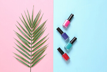 Obraz premium Bottles of nail polish and palm leaf on blue pink background. Beauty still life. Top view. Flat lay