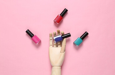 Obraz premium Wooden hand holding nail polish bottles on pink background