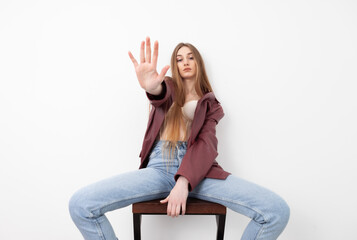 Obraz premium Fashionable vogue woman model dressed in jeans, leather jacket and corset sitting on chair, white background