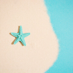 Fototapeta na wymiar Starfish laid out on sand on blue backgorund. Summer beach concept. Miniimal flat lay.