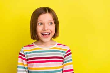 Photo of happy cheerful amazed little girl look empty space good mood smile isolated on yellow color background