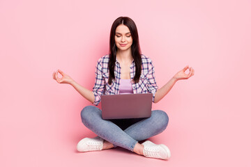 Portrait of attractive dreamy focused girl sitting lotus pose meditating using laptop isolated over...