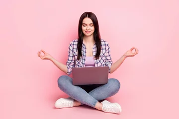 Foto op Canvas Portrait of attractive dreamy focused girl sitting lotus pose meditating using laptop isolated over pink pastel color background © deagreez