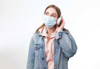 Young woman in medical mask listening to music on headphones isolated on white background
