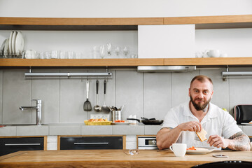 White man with beard having lunch while sitting at table in kitchen