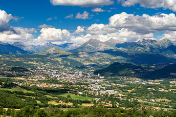 Fototapeta na wymiar The city of Gap in Summer with view of the distant mountains of the Ecrins National Park massif. Hautes-Alpes in the French Alps. France