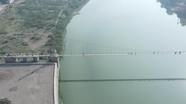 Drone flies high in the sky above floating clouds. Below, overlooks an impressive view of the Hanging bridge near machhu dam, Aerial. 4K