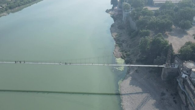 Drone flies high in the sky above floating clouds. Below, overlooks an impressive view of the Hanging bridge near machhu dam, Aerial. 4K