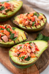 Grilled avocado stuffed with tuna, tomatoes, parsley, and olive oil on a cutting board. 