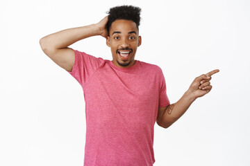 Fototapeta premium Portrait of handsome african american man in pink t-shirt, touch head and look surprised, pointing finger right at sale logo, showing banner, white background