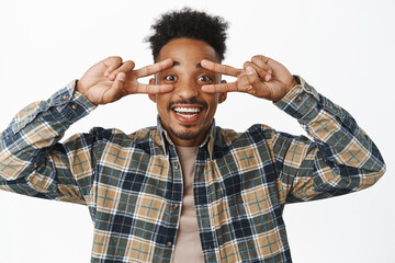 Close up portrait of positive, smiling african american male student, guy showing peace v-sign...