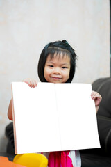 Mock up learning book. Asian child girl standing holding to show working book. Kid sweet smiling with homework. Vertical image. Children aged 4-5 years old. Education at home. Homeschool.