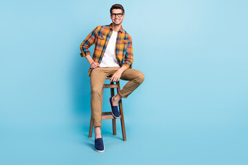 Photo of attractive cute gentleman wear checkered shirt arm glasses sitting bar chair empty space isolated blue color background