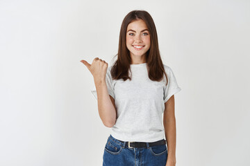 Beautiful female student making her choice and pointing thumb left, showing company logo or banner, standing over white background