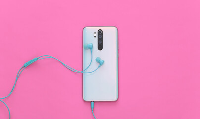 Smartphone and earphones on pink background. Top view