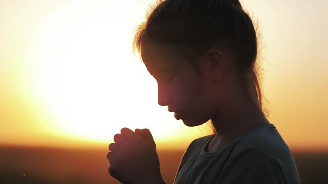 Child praying at sunset, thank God. Silhouette child praying to the God with bright sunbeam on the sky. Religion concept.
