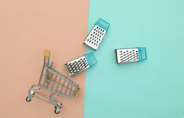 Supermarket trolley with mini graters on pink blue pastel background. Top view