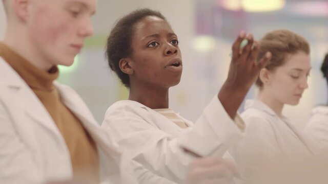 Medium side-view slowmo of young Afro American female medial student chatting with classmates during lecture asking them questions about new topic