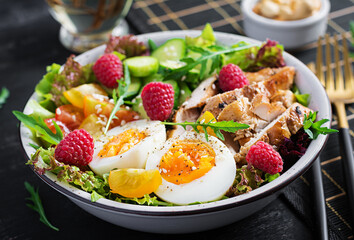Grilled chicken meat and fresh vegetable salad of tomato, cucumber, egg, lettuce and raspberry. Ketogenic diet. Buddha bowl dish on dark background
