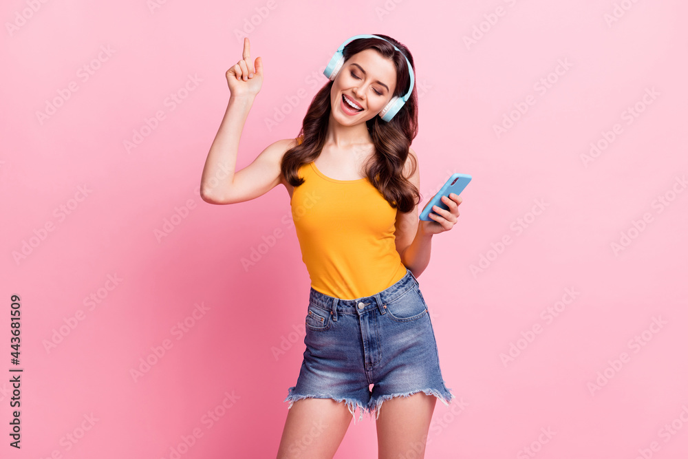 Wall mural Photo of adorable sweet young woman wear yellow singlet listening music holding modern gadget isolated pink color background