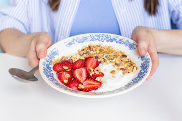 Woman's hands holding homemade granola with fresh organic strawberries and yogurt in the vintage plate. Morning breakfast food concept