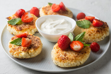 Cottage cheese pancakes with strawberries, mint and sour cream on a light background. syrniki. healthy dessert