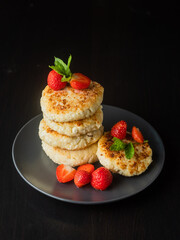 Cottage cheese pancakes with strawberries, mint and sour cream on a black background. syrniki. healthy dessert