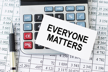 Everyone Matters inscription on a white card that lies on a calculator with a pen and financial...