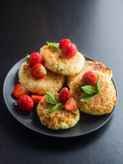 Cottage cheese pancakes with strawberries, mint and sour cream on a black background. syrniki. healthy dessert