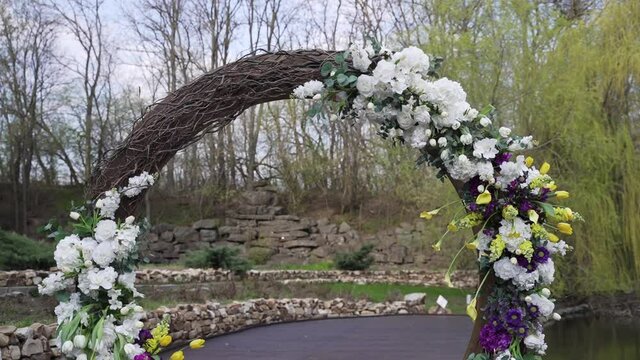 Round wedding arch decorated with flowers stands at wedding ceremony on the street. White flowers and yellow tulips