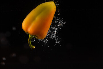 yellow bell pepper dropped into the water on a black background and a lot of bubbles