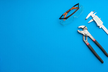 Technician's set of tools on solid coloured blue background including spectacles, caliper and pliers