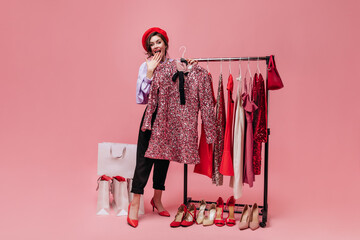 Girl in hat in joyful surprise holds hanger with shiny dress. Portrait of woman at time of shopping...