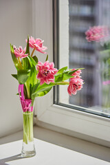 Delicate pink tulips in a vase on the windowsill on a sunny day.