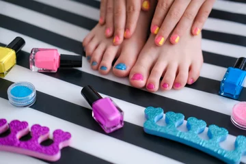 Zelfklevend Fotobehang Children's feet with bright pedicure and manicure of different colors and bottles of bright nail polish. Little girl does a pedicure. Beauty salon game. Children is entertainment. © smile35