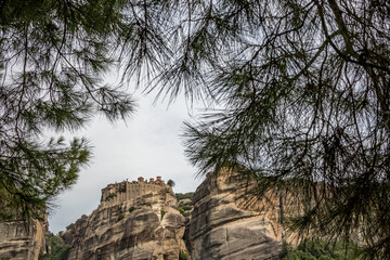 Obraz premium Meteora, Greece, low angle perspective of one monastery on a cliff high in the sky. Framed view by pine tree branches and needles.