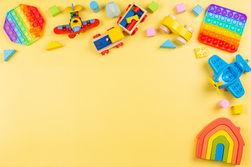 Fototapeta na wymiar Baby kid toys background with wooden blocks, train, car, plane, pop it fidget toy on yellow background. Top view, flat lay, copy space