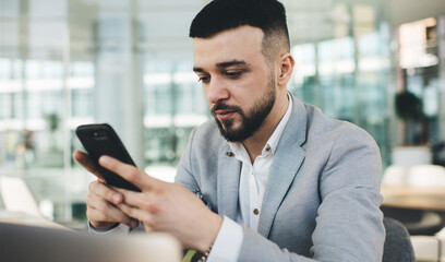 Crop serious businessman browsing smartphone in glass office