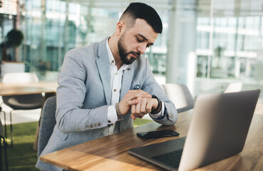 Serious businessman checking time on wristwatch in office
