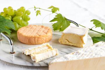 Delicious cheese brie or camembert on cutting board with bunch of grape on the table with white tablecloth. Dairy products. Italian, French cheese. Breakfast. Selective focus