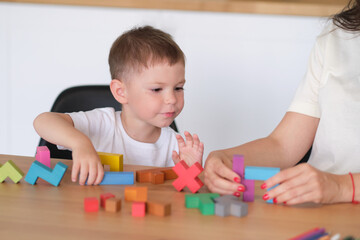 Fototapeta premium kid boy and mother playing educational toys at table at home. child's playing with colorful wooden bricks at the table.