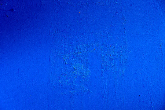 An old metal wall painted with a new blue paint similar to the color of the sea. There is uneven illumination of the surface. The texture of the previous layers of paint and glue comes in. Background.