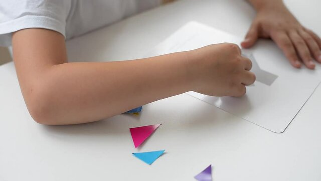 A preschooler girl sitting at the table collects a drawing from a geometric figure. the concept of early childhood development by montessori. a game of logic and imagination