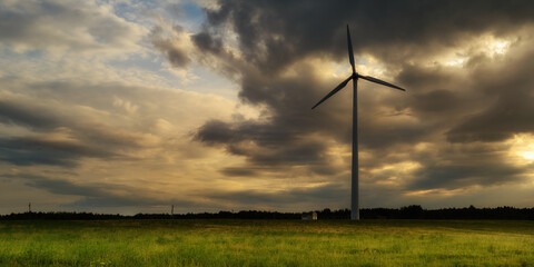 wind power plant in a wide agricultural field against the backdrop of a dramatic evening cloudy sky. beautiful panoramic industrial landscape with copy space