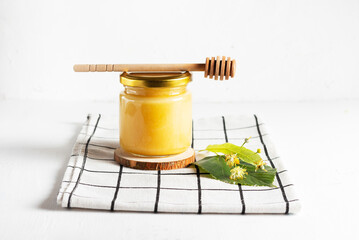 Fresh lime honey in a glass jar with a wooden honey spoon on a white napkin in a high key