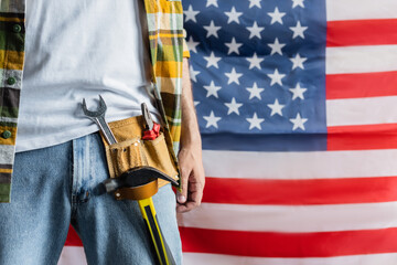 partial view of builder in tool belt near usa flag on blurred background, labor day concept